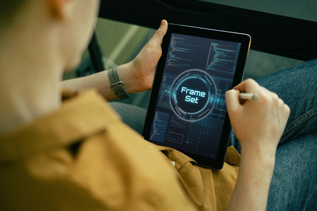 A person in a tan shirt and blue jeans holds a tablet with a stylus, showing a futuristic digital interface on the screen.