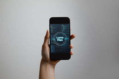 A hand holding a black smartphone against a plain light gray background. The phone screen displays a futuristic blue interface with the text 'Luma Plan'.